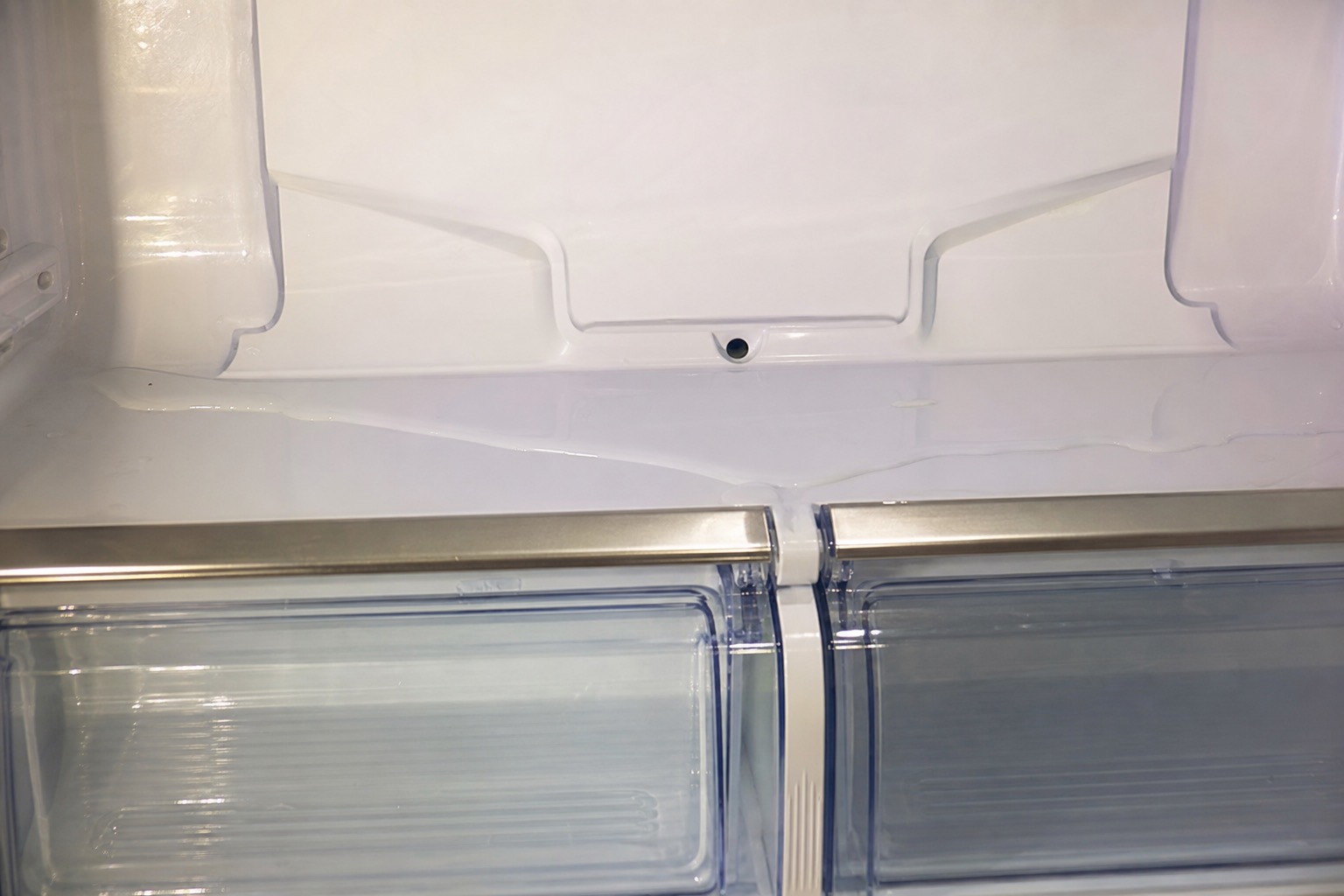 Close view of a refrigerator defrost drain area with water near the lower drawers