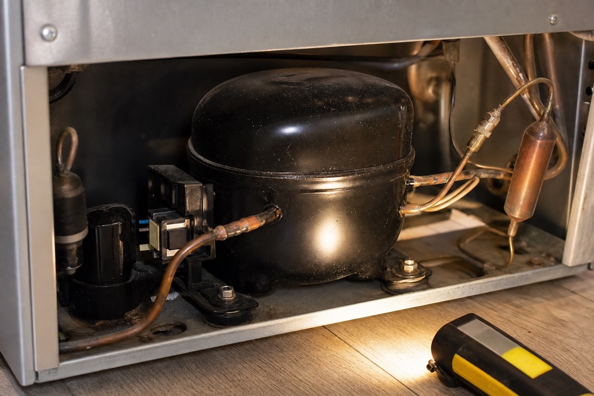 Close view of refrigerator compressor and start components lit by a work light