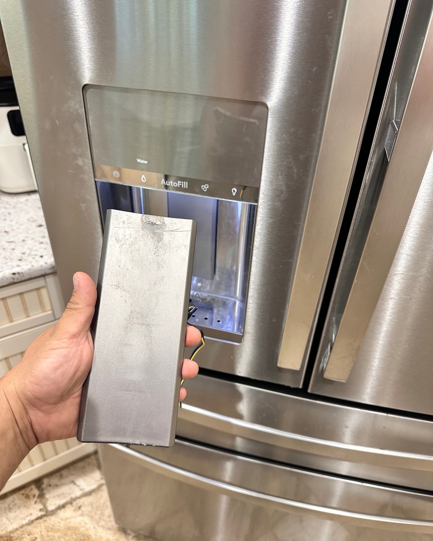 Removed dispenser paddle held in front of the GE refrigerator.