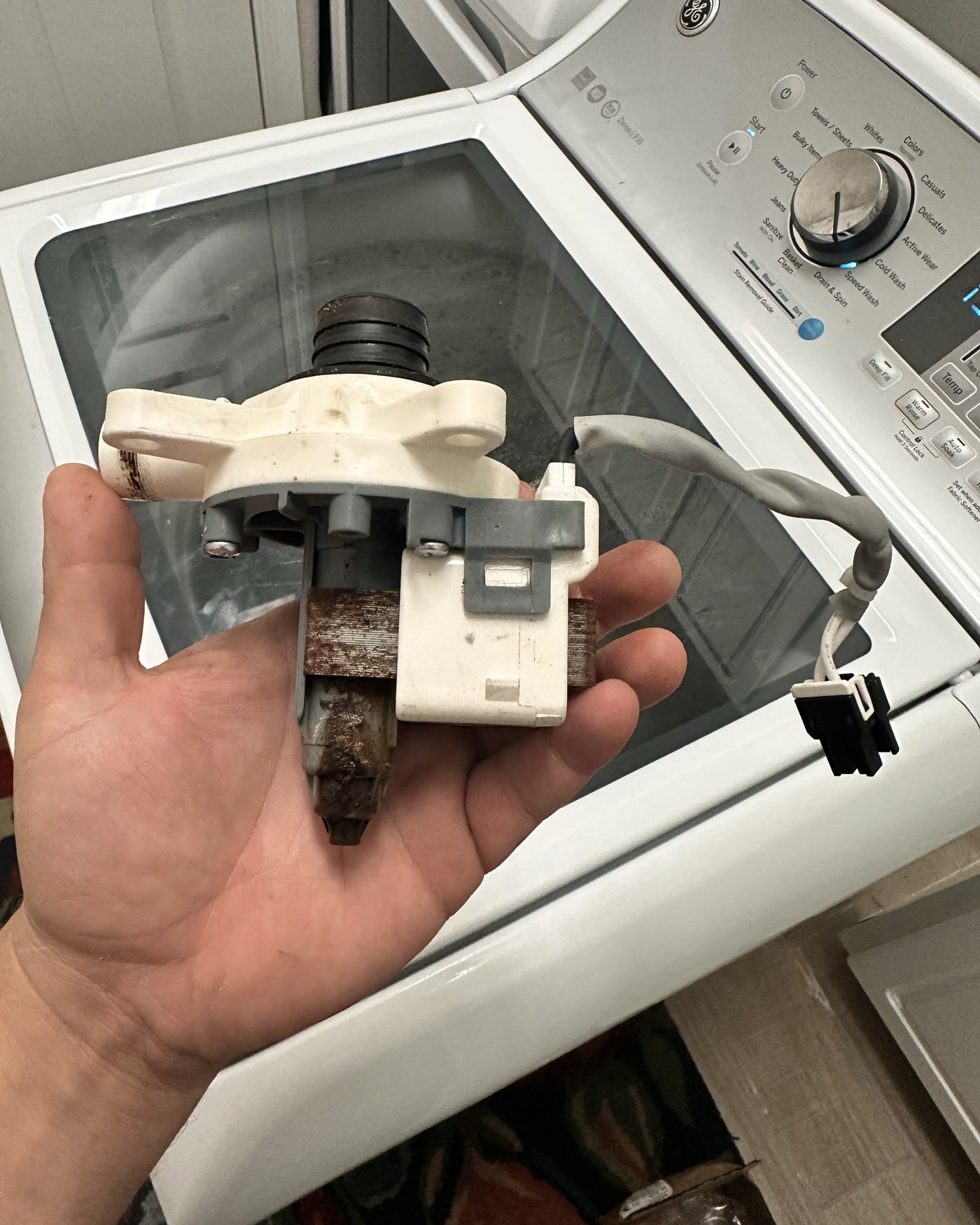 Removed circulation pump held above a GE top-load washer.