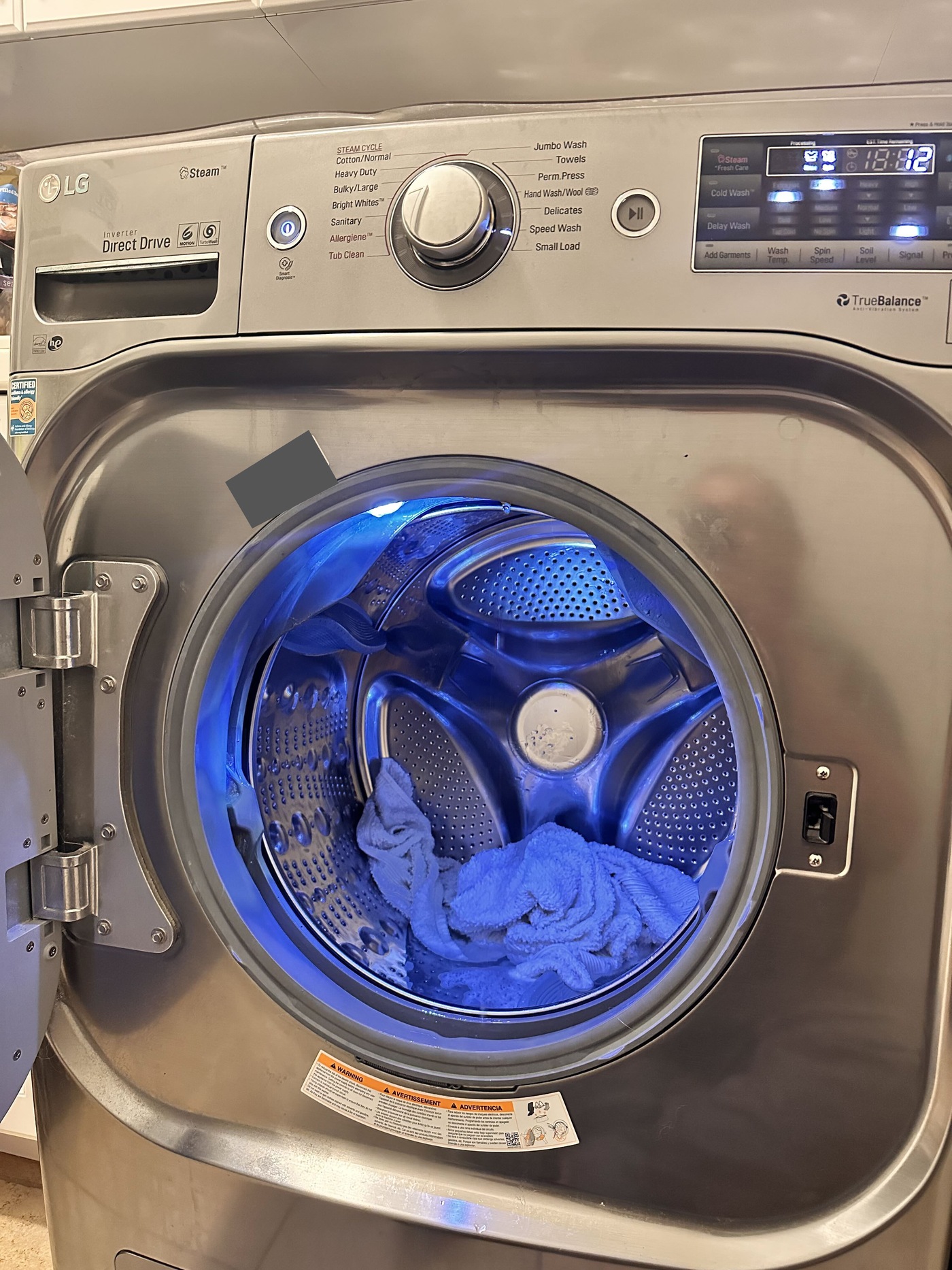LG WM8100HVA front-load washer with the door open, control panel visible and towels inside the drum; identification label obscured for privacy.