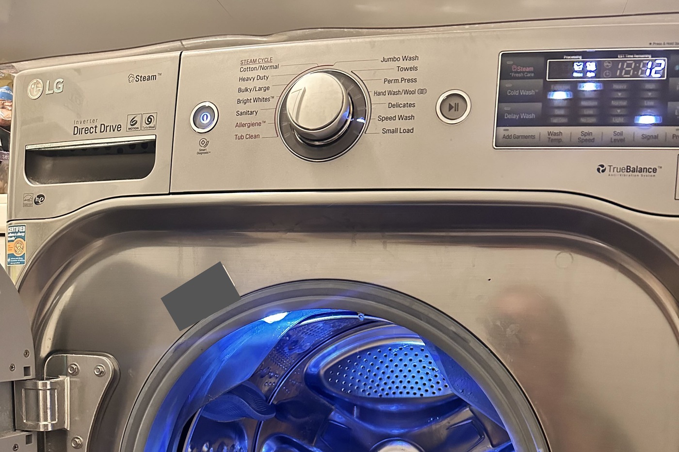 Control panel and open drum of the LG WM8100HVA front-load washer; identification label obscured.
