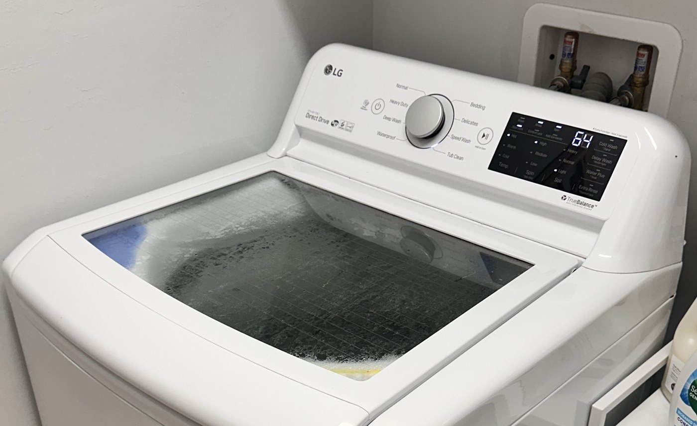 LG WT7100CW washer with the glass lid closed and control panel visible.
